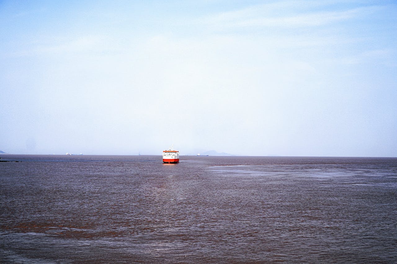 Distant cargo ship sailing on a vast, calm sea under a clear, blue sky.